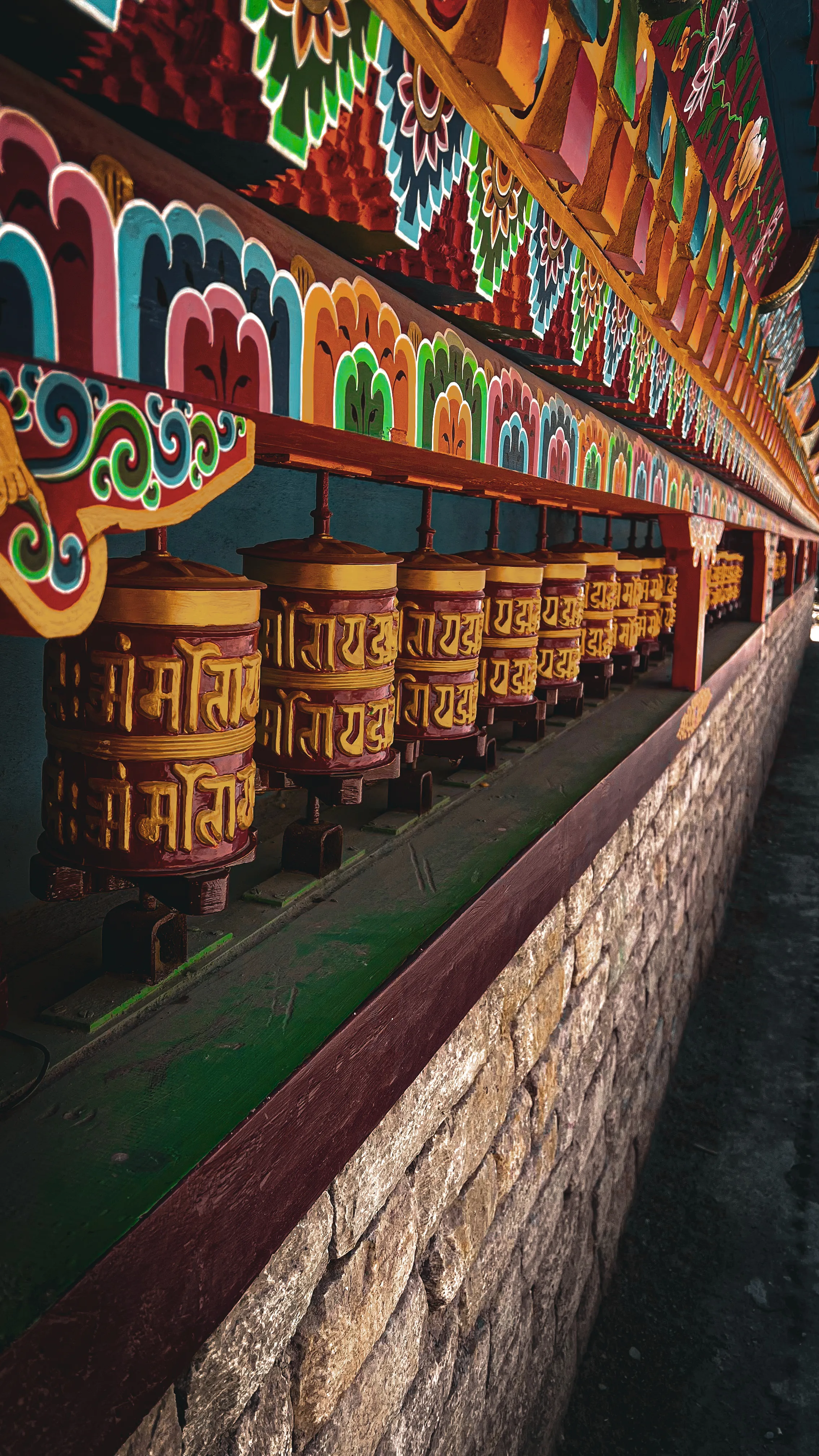Colorful Buddhist prayer wheels with golden Sanskrit inscriptions at a Himalayan monastery