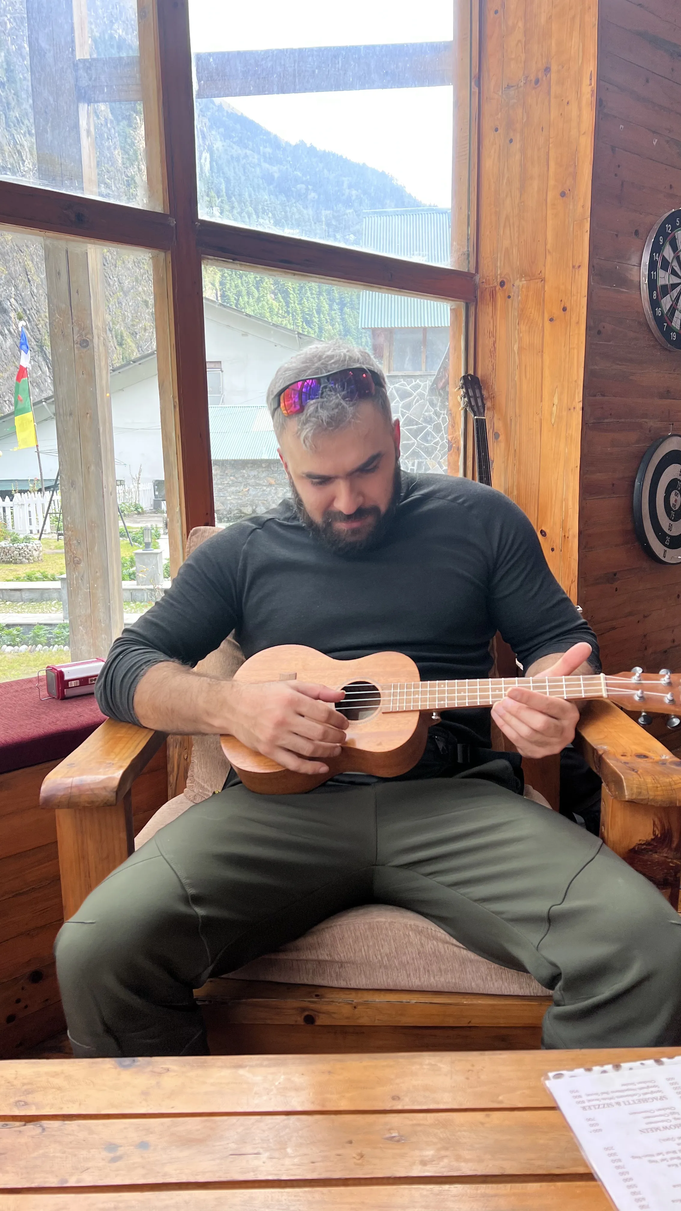 Ian Gabaraev playing ukulele inside a Himalayan teahouse with mountain view through the window